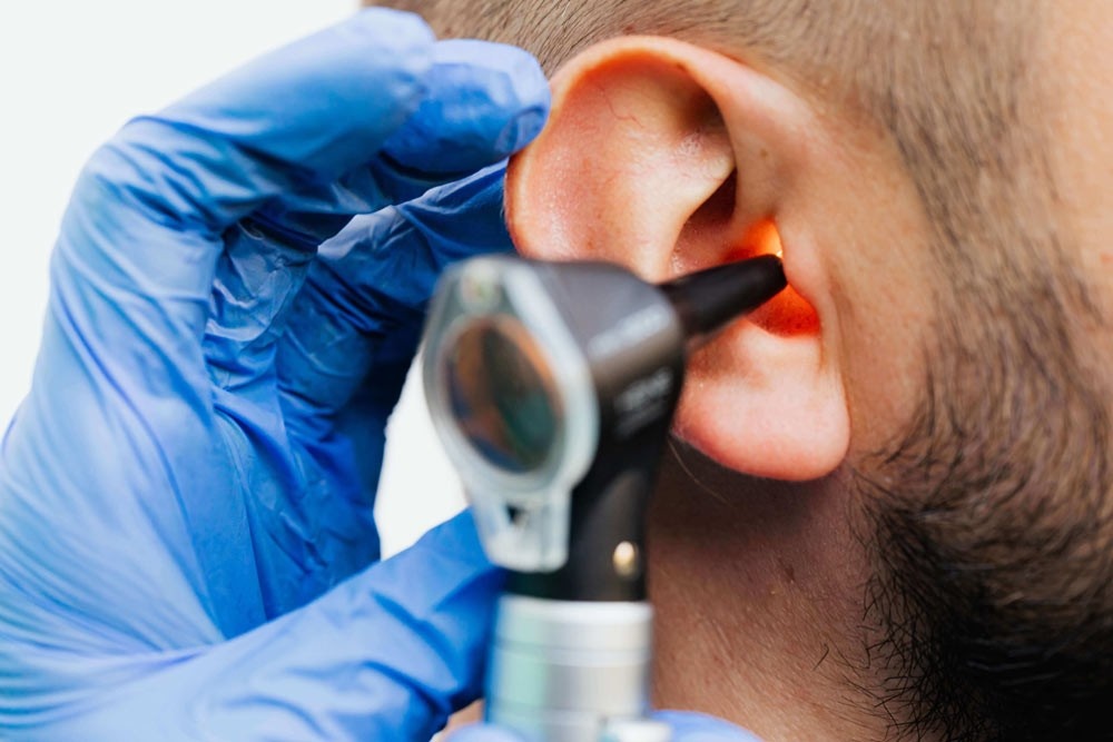 Close-up of doctor examining patient’s ear with otoscope for earwax buildup.